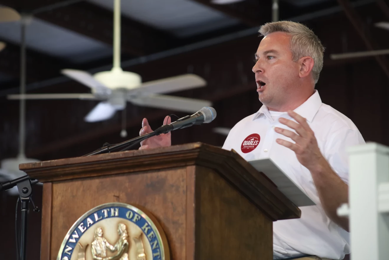 Ryan Quarles stands behind a lectern with the state seal of Kentucky on the front. He wears a white, collared shirt and speaks into a microphone. 